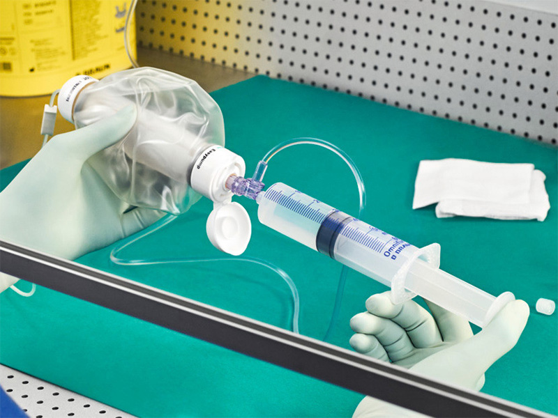 gloved hands holding a half full syringe connected to a portable soft balloon pump for filling