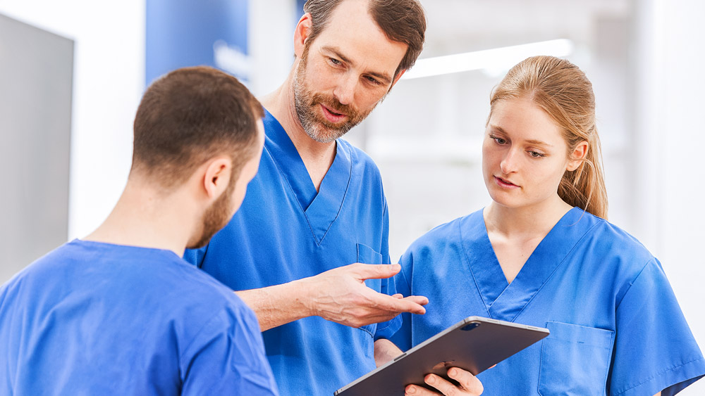 Three doctors discuss something on a tablet