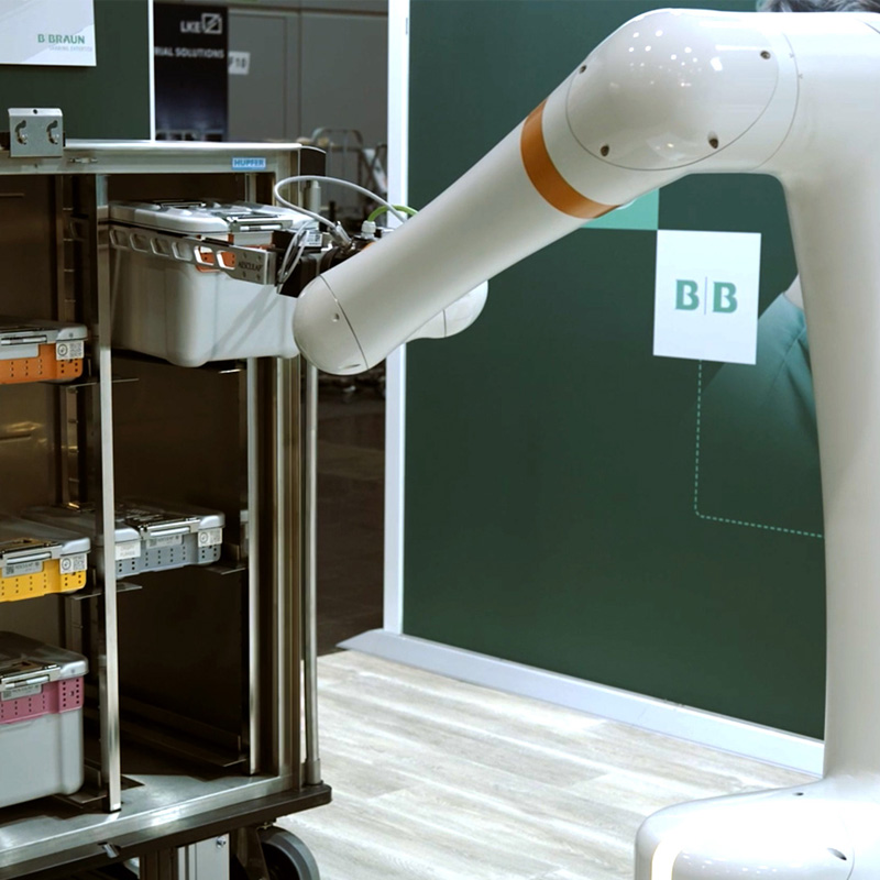 Robotic arm removes a AESCULAP sterile container from a transport cart and supports automated logistics processes within Central Sterile Supply Department