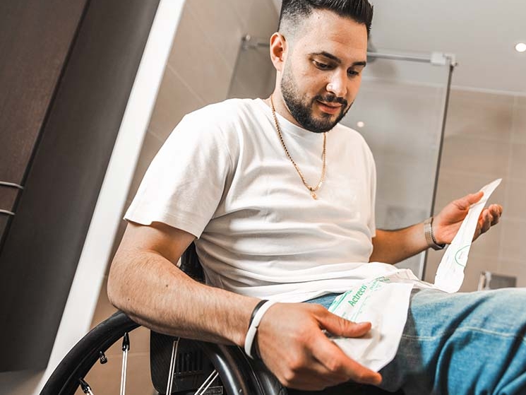 A man in a wheelchair, a bathroom in the background, holding a cathether in his hand