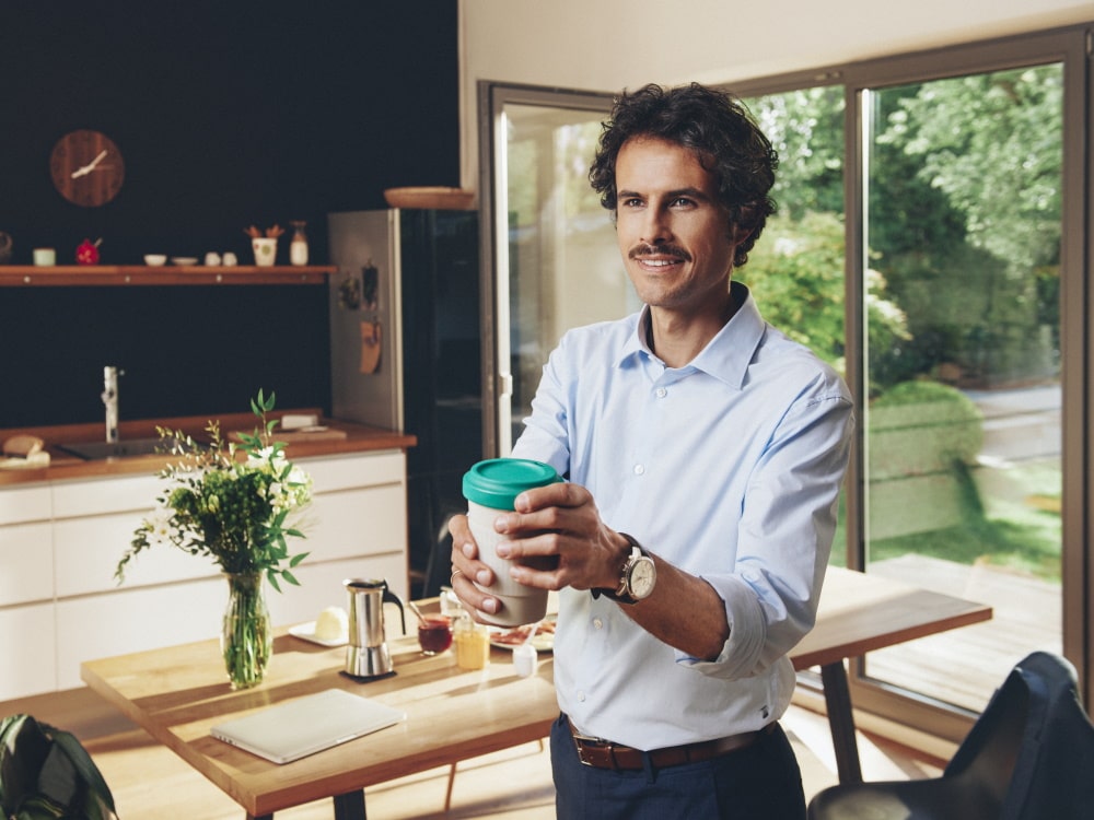 A man is standing in a private house, holding a cup of coffee