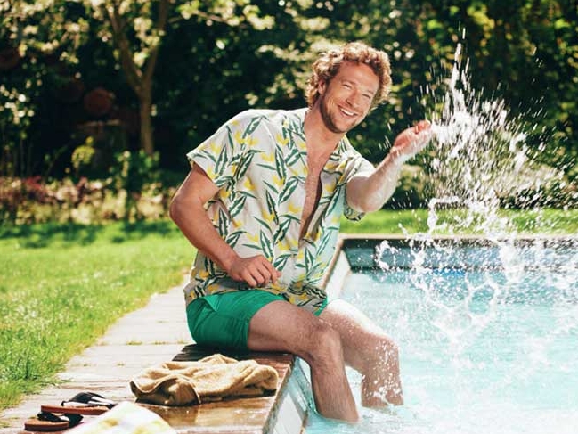 A young man is sitting next to the swimming pool, splashing the water with his hand