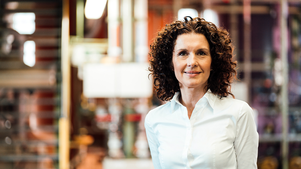 A woman with curly hair standing gracefully in front of a sleek glass wall. 