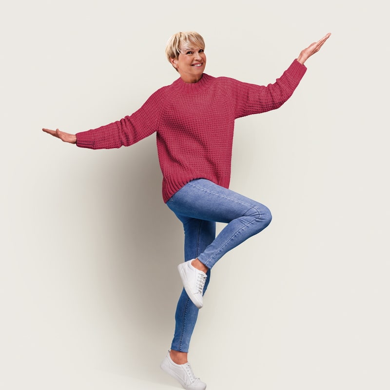blond woman with red pullover who bends one leg and stretches out both arms