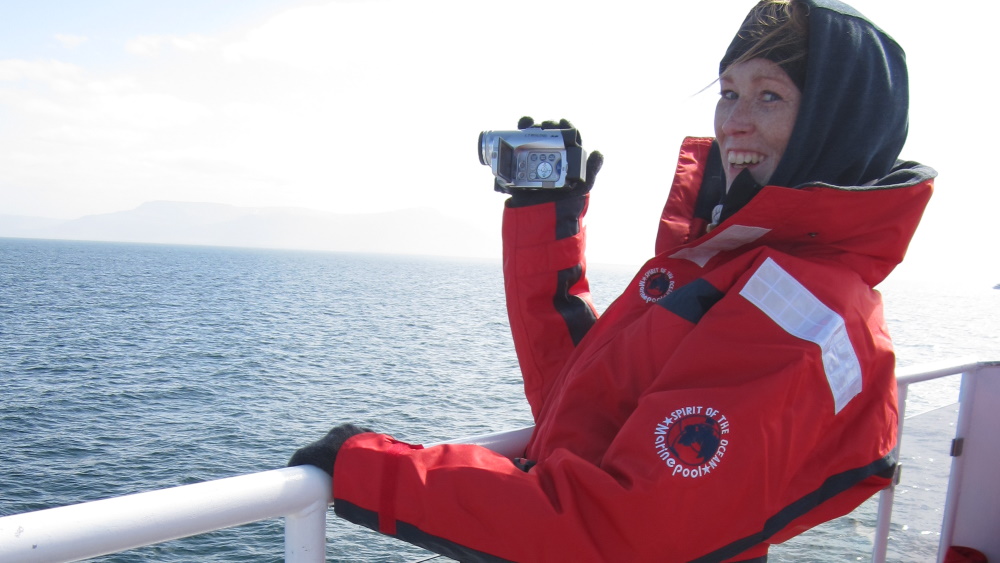 Woman with thick winter coat and hood who holds a camera on a boat