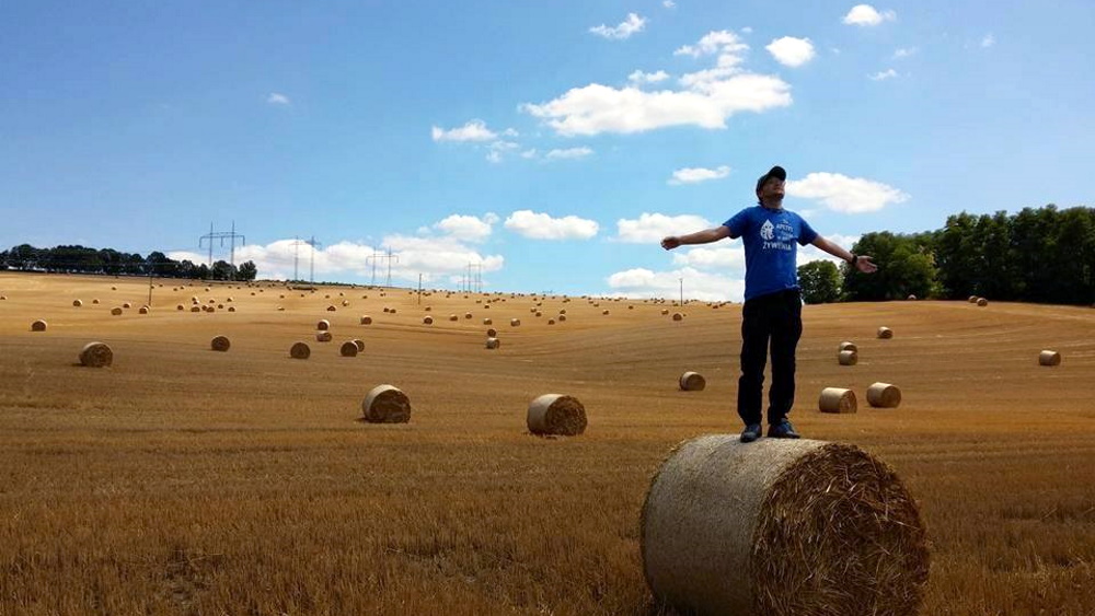Man with cap who stands on a straw round bale and spreads his arms