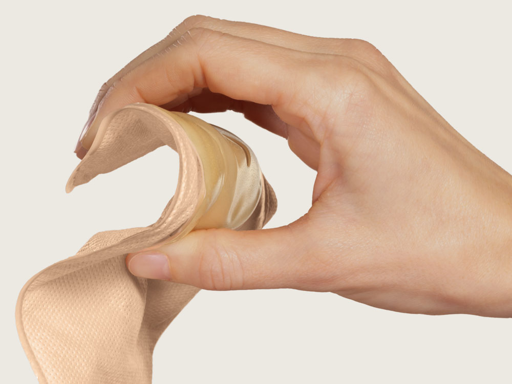 Hand presses the wafer of a soft convex stoma bag to demonstrate its flexibility